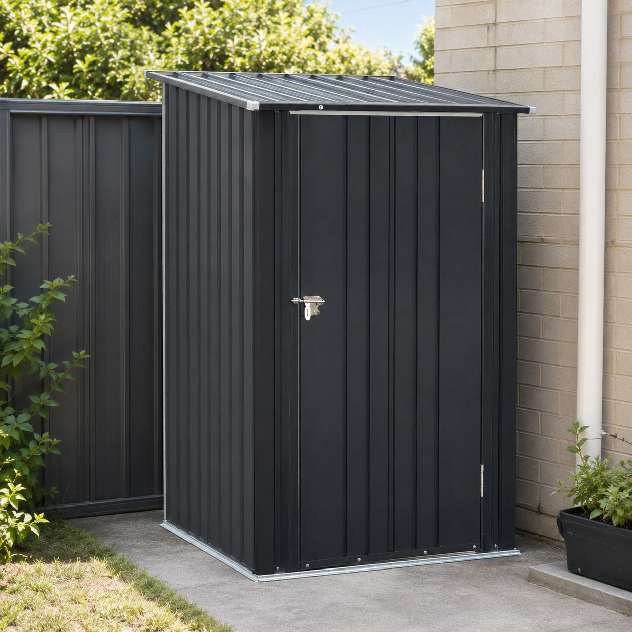 A black metal garden shed with a single door and silver latch, positioned outdoors next to a beige brick wall and green plants.