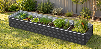 A rectangular raised garden bed with a dark gray corrugated metal exterior and silver interior dividers, filled with various green herbs and plants, situated on a green lawn in a backyard setting.