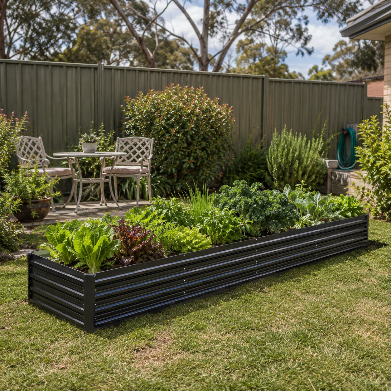 Garden with raised bed filled with vegetables, outdoor seating area, and trees in the background.