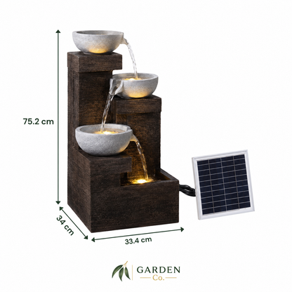 A three-tier solar-powered waterfall fountain with dark brown wood-look steps and gray stone bowls, shown with dimension labels and a small solar panel on a white background. Garden Co.
