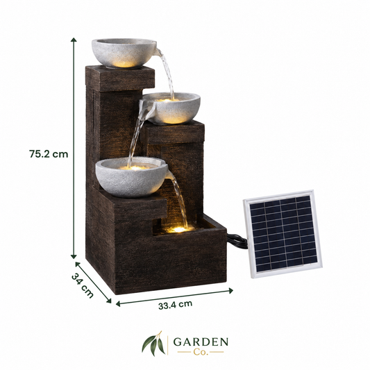 A three-tier solar-powered waterfall fountain with dark brown wood-look steps and gray stone bowls, shown with dimension labels and a small solar panel on a white background. Garden Co.
