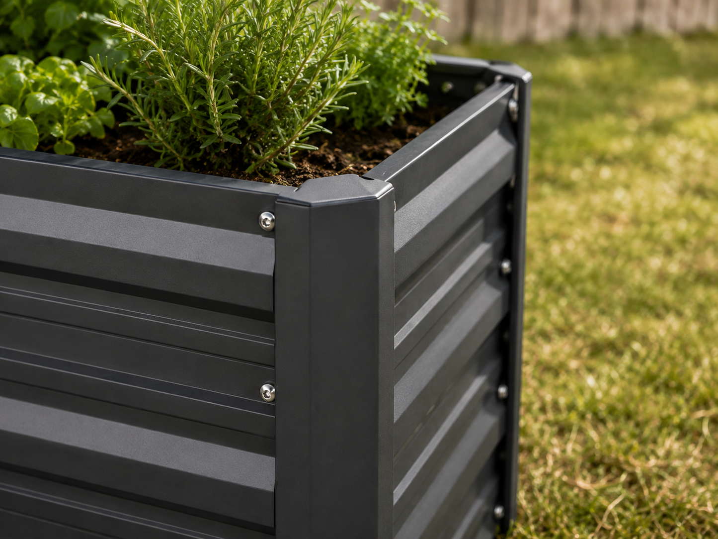 A dark gray metal raised garden bed with horizontal slats, filled with green plants, shown outdoors on a grassy lawn.