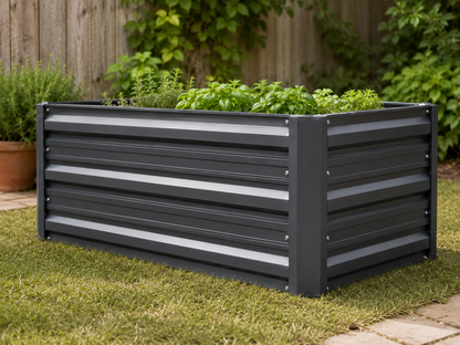 A rectangular raised garden bed with dark gray horizontal slats, filled with green herbs, set on a grassy lawn in a backyard with a wooden fence and plants in the background.