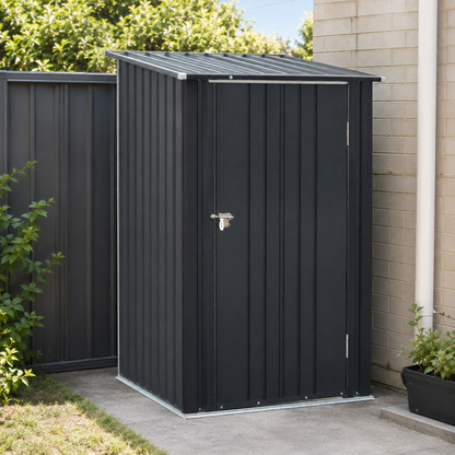 A black metal garden shed with a single door and silver latch, positioned outdoors next to a beige brick wall and green plants.