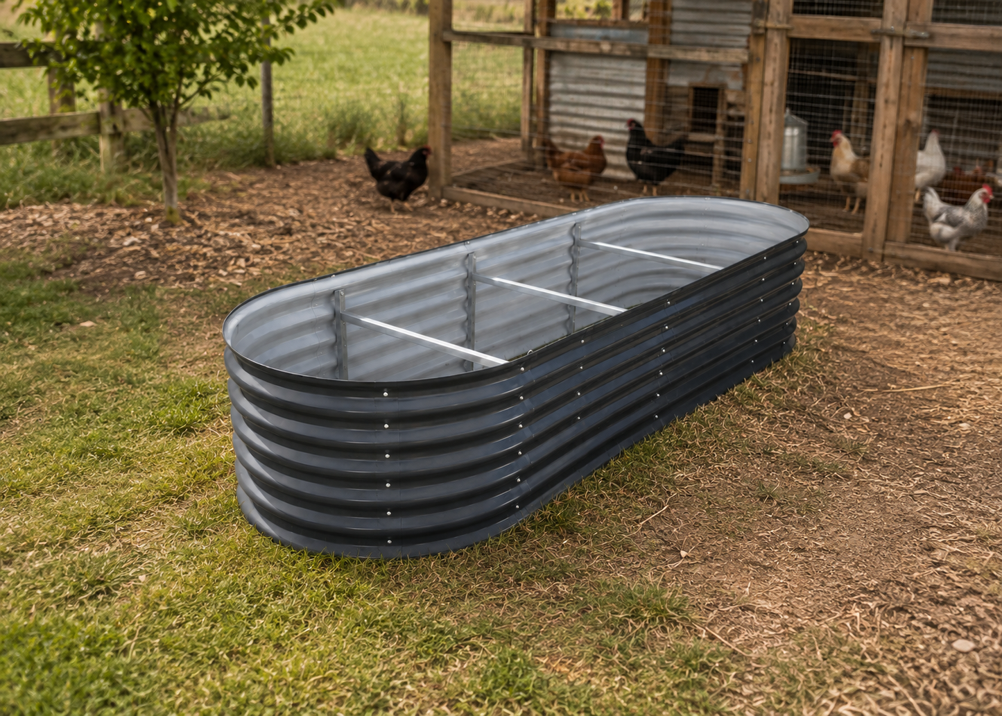 A corrugated metal chicken trough with a slotted top, placed on grass in a backyard with chickens visible in the background.