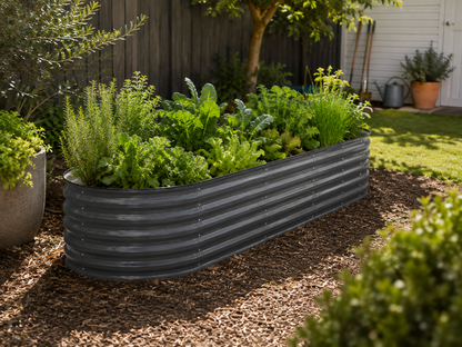A dark gray corrugated metal raised garden bed filled with leafy greens and herbs, situated on a bed of brown mulch in a backyard garden setting.