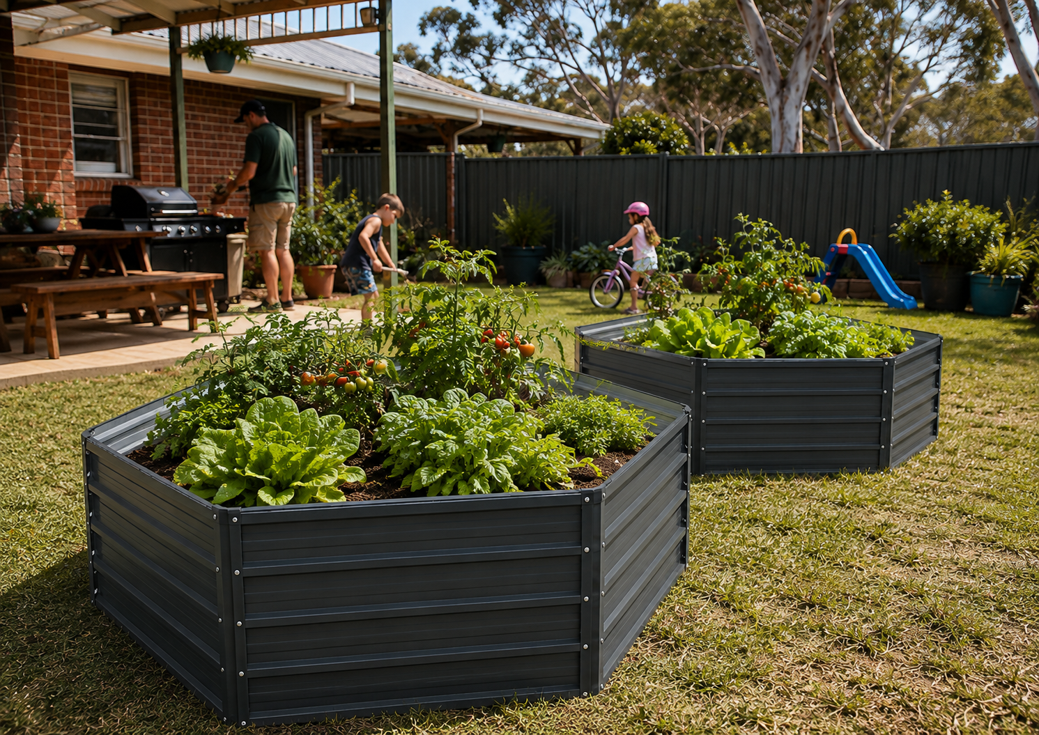 Two dark gray hexagonal raised garden beds filled with leafy green plants in a backyard lawn, with people and a child playing in the background near a house and fence.