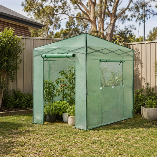 A green fabric pop-up garden tent with a roll-up door and side window, set up on a grassy backyard lawn next to a wooden fence and potted plants.