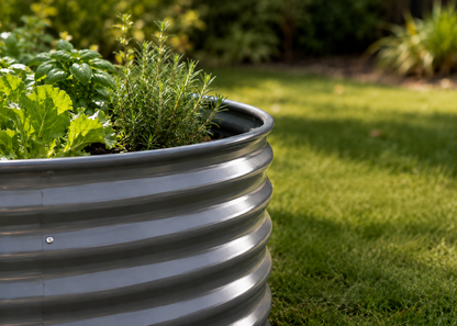 A corrugated galvanized steel raised garden bed filled with green herbs and leafy plants, set on a sunny green lawn.