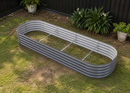 A long, corrugated metal raised garden bed on a grassy backyard lawn with a black fence and potted plants in the background.
