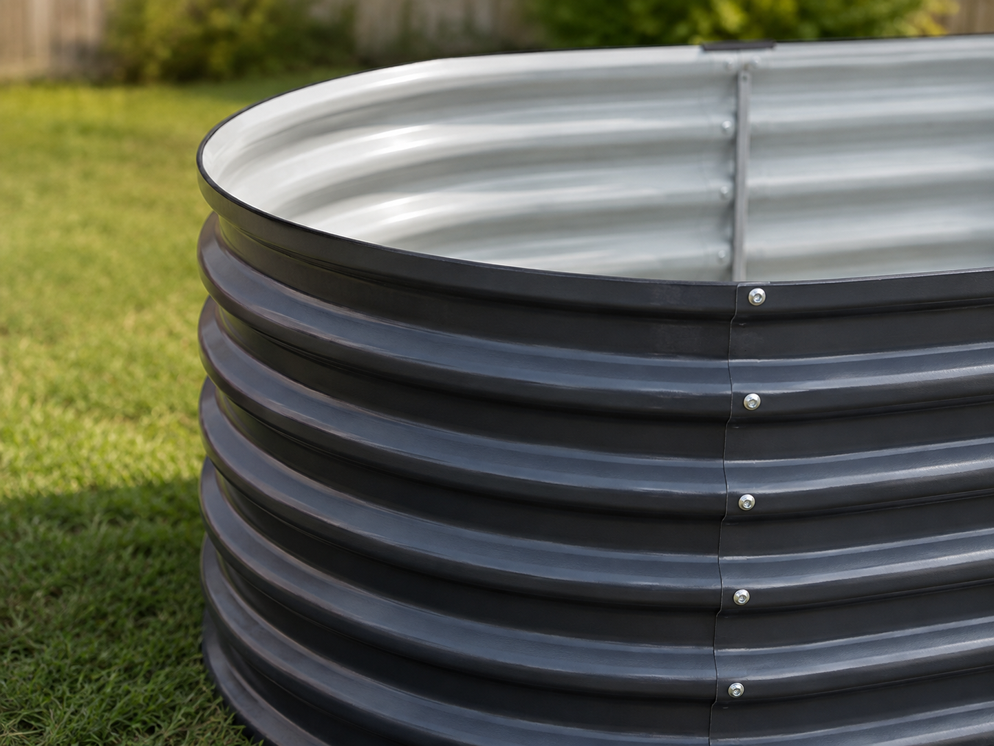 A galvanized steel corrugated round water tank with a dark gray outer wall and silver inner lining, shown outdoors on a green grass lawn.