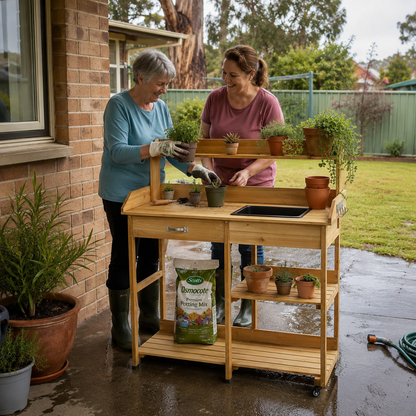 Two women tending to plants on a wooden outdoor kitchen cart in a garden setting.