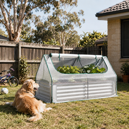A small pop-up greenhouse with corrugated metal sides and mesh top, set in a backyard on grass next to a golden retriever dog. The greenhouse contains leafy green plants, with a wooden fence, trees, and part of a house visible in the background.