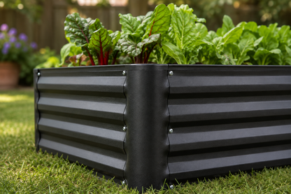 A black corrugated metal raised garden bed filled with leafy green vegetables, set on a green lawn in an outdoor garden setting.