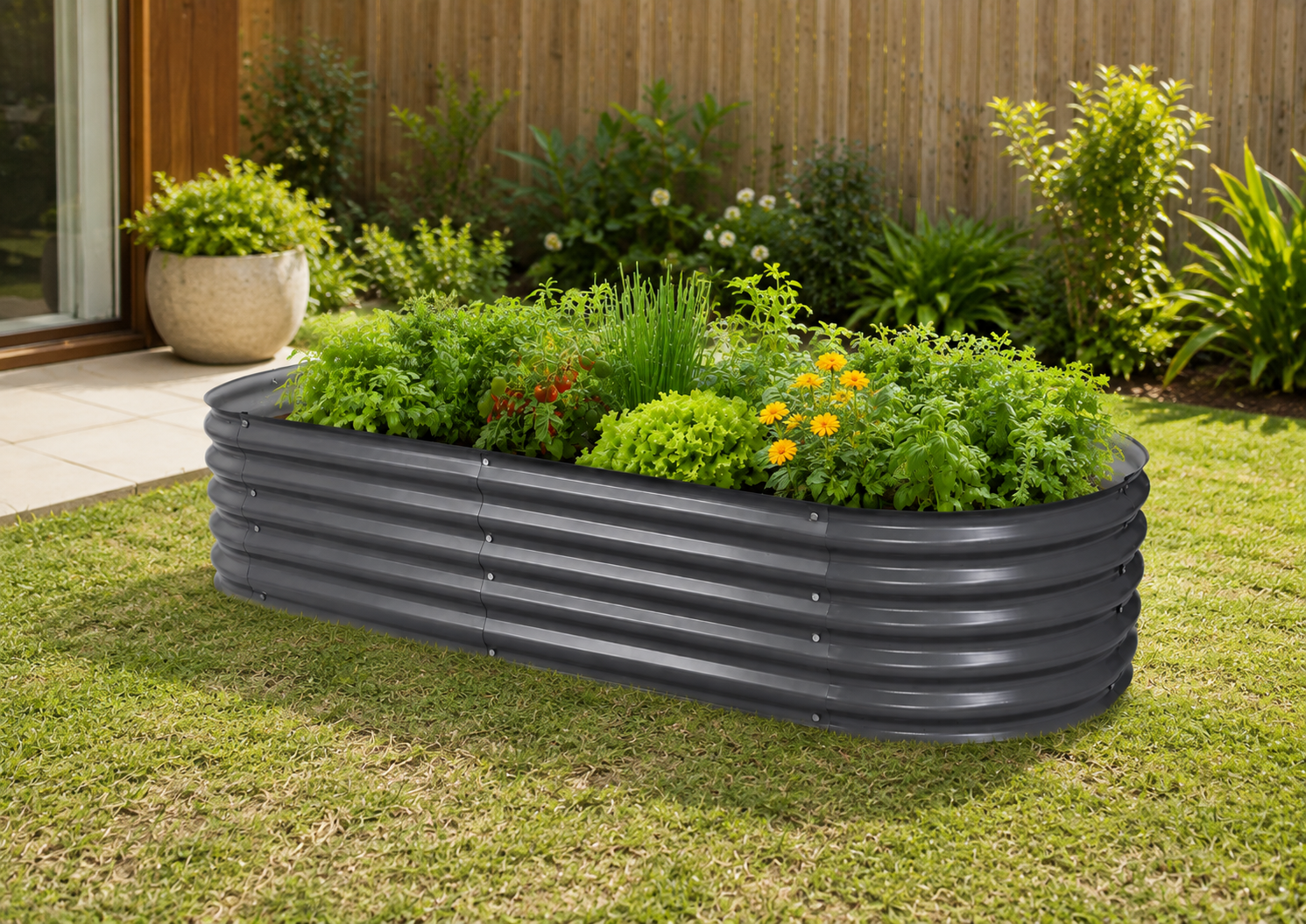 A dark gray corrugated metal raised garden bed filled with green plants and small yellow flowers, placed on a grassy lawn in a backyard garden setting.