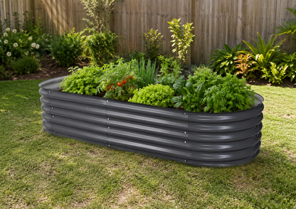 A dark gray corrugated metal raised garden bed filled with green plants, situated on a grassy lawn in front of a wooden fence.