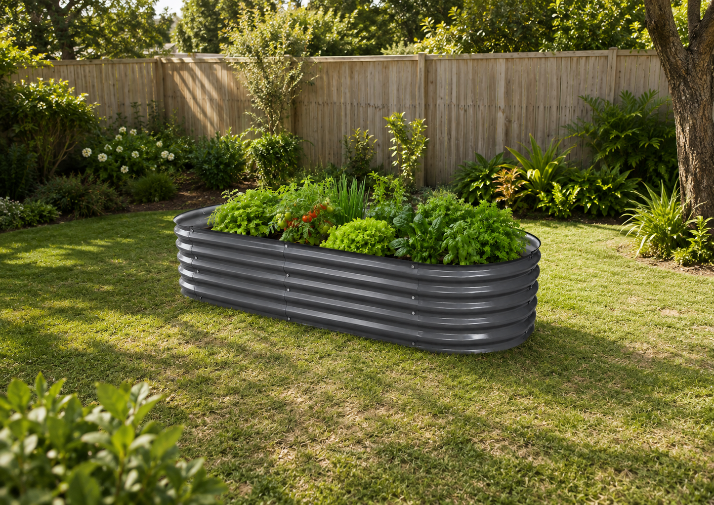A dark gray corrugated metal raised garden bed filled with green plants, situated on a grassy lawn in a backyard with a wooden fence and trees in the background.