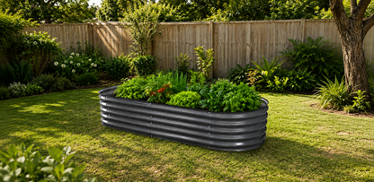A dark gray corrugated metal raised garden bed filled with green plants, situated on a grassy lawn in a backyard with a wooden fence and trees.