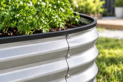A close-up of a galvanized steel raised garden bed with a corrugated metal design, black rim, and visible silver rivets, filled with green leafy plants in soil, set outdoors on grass with a blurred garden background.