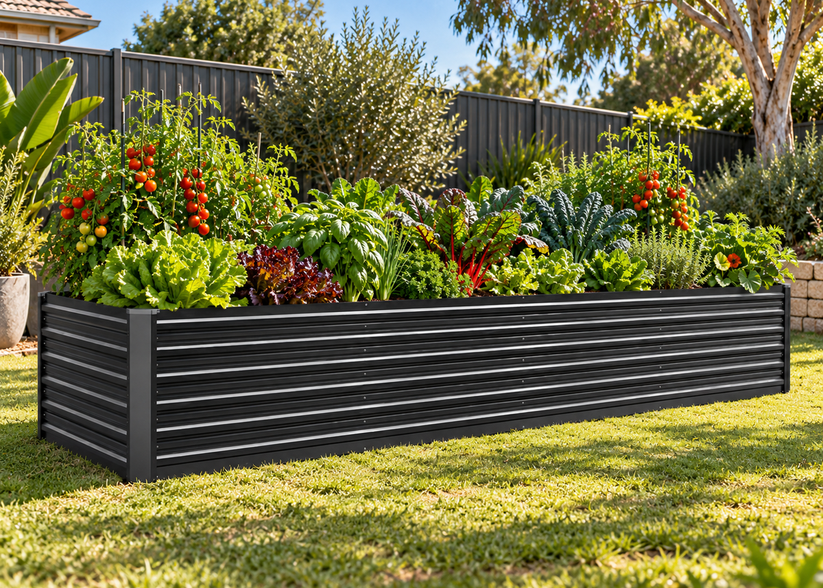A rectangular black metal raised garden bed with horizontal slats, filled with leafy greens, red chili plants, and tomatoes, situated on a green lawn in a backyard setting.