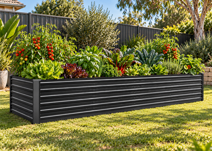 A rectangular black metal raised garden bed with horizontal slats, filled with leafy greens, red chili plants, and tomatoes, situated on a green lawn in a backyard setting.