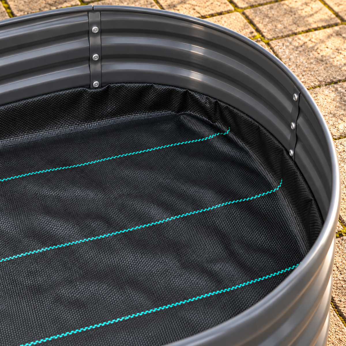 Close-up of a round black metal planter or tub with a black mesh liner inside, featuring bright teal stitched lines and visible mounting screws on the rim, photographed outdoors on a paved surface.