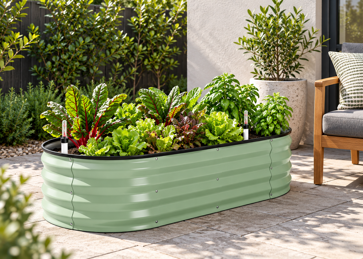 Compact green self-watering raised garden bed planted with leafy greens beside an outdoor chair and pot plant.
